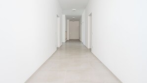 Un pasillo largo y estrecho con paredes blancas y piso de baldosas claras.