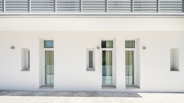 Fachada de edificio moderno con tres ventanas rectangulares, cada una con un pequeño alero y una puerta visible.