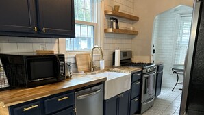 A modern kitchen with dark cabinets, a stainless steel refrigerator, a microwave, and a dishwasher. - Charming 1925 Home In Broad Ripple - Sleeps 6, Modern Comforts & Prime Location (Indianapolis)