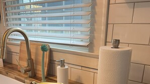 A kitchen counter with a wooden bowl containing bananas and apples, a paper towel dispenser, and a faucet. - Charming 1925 Home In Broad Ripple - Sleeps 6, Modern Comforts & Prime Location (Indianapolis)