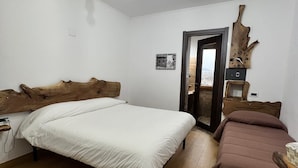 Une chambre à coucher avec une tête de lit en bois, un lit, un canapé marron, une horloge murale en bois et une porte donnant sur une autre pièce.