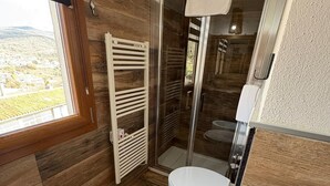Une salle de bain avec un plancher en bois, un bidet, des toilettes et une douche dotée d’une porte en verre.