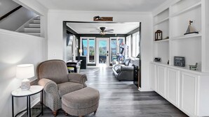 Un pasillo amplio con un sillón tapizado gris, una mesita redonda con una lámpara y un ventilador de techo.