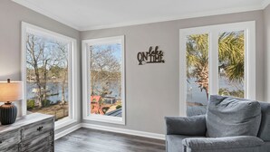 Una habitación con ventanas amplias, un sofá gris, un armario de madera y un letrero en la pared.