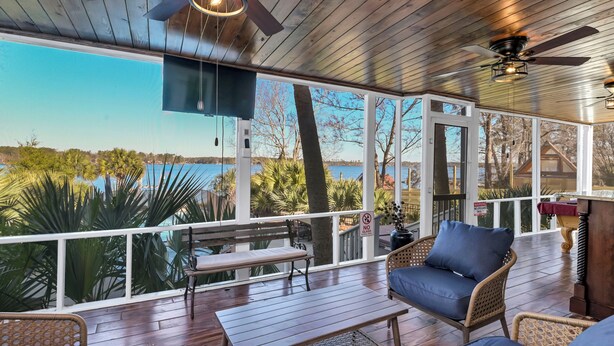 Una terraza techada con suelo de madera, ventilador de techo, televisor y vista al agua.