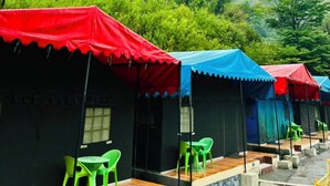 A row of tents with red and blue canopies, green plastic chairs, and a hilly landscape in the background. - Baromas Resort and Camping (Chakrata)