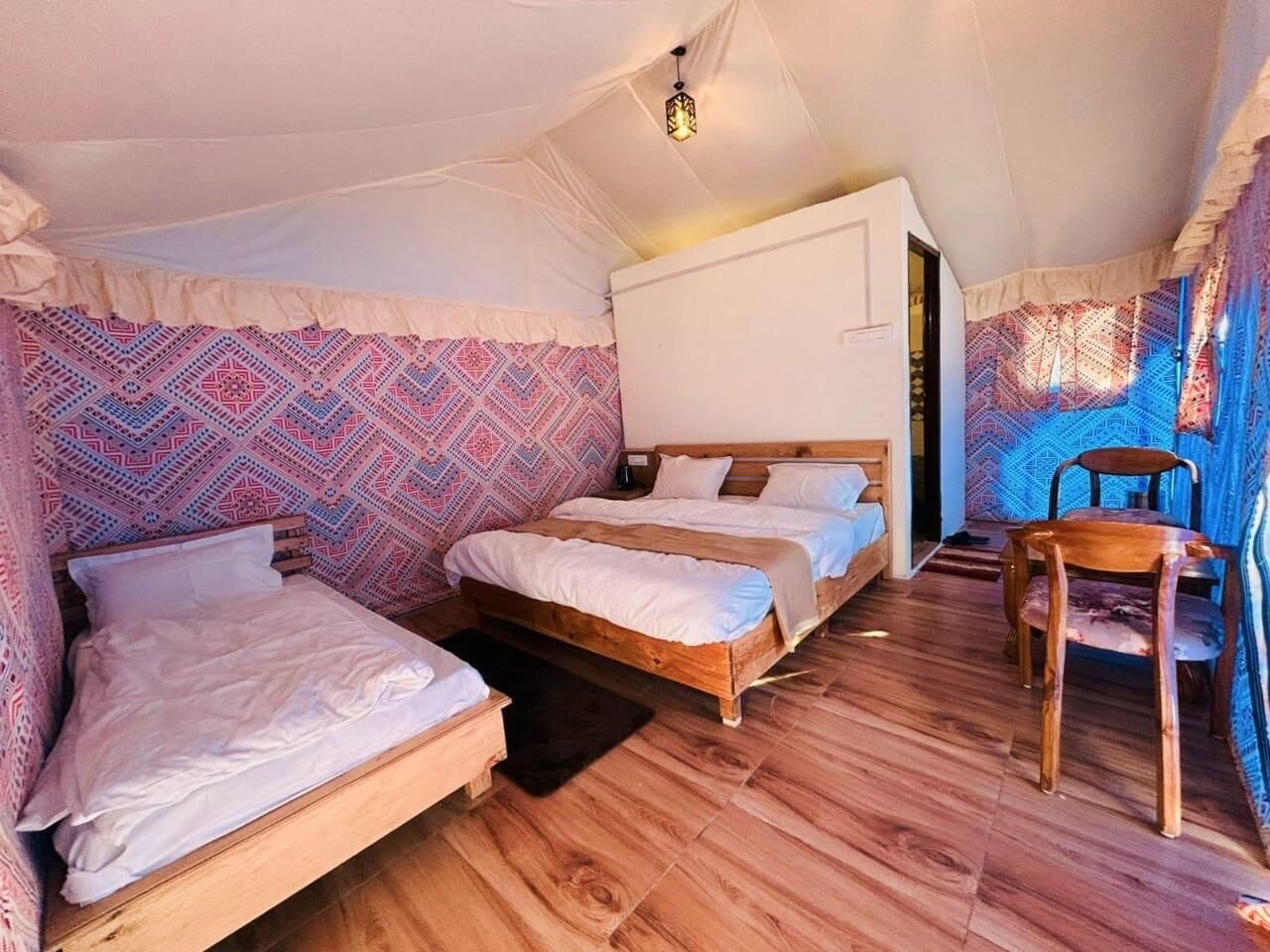 A cozy tent-style room with two wooden beds, a small table, and a chair.