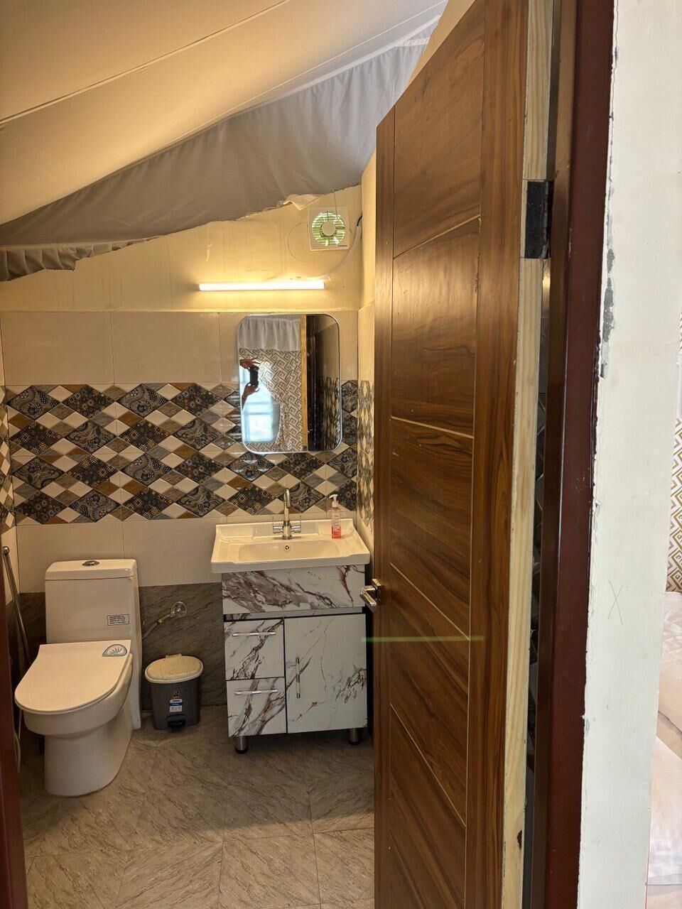 Ein Badezimmer mit Toilette, Waschbecken, Spiegel und Wandfliesen mit Muster.