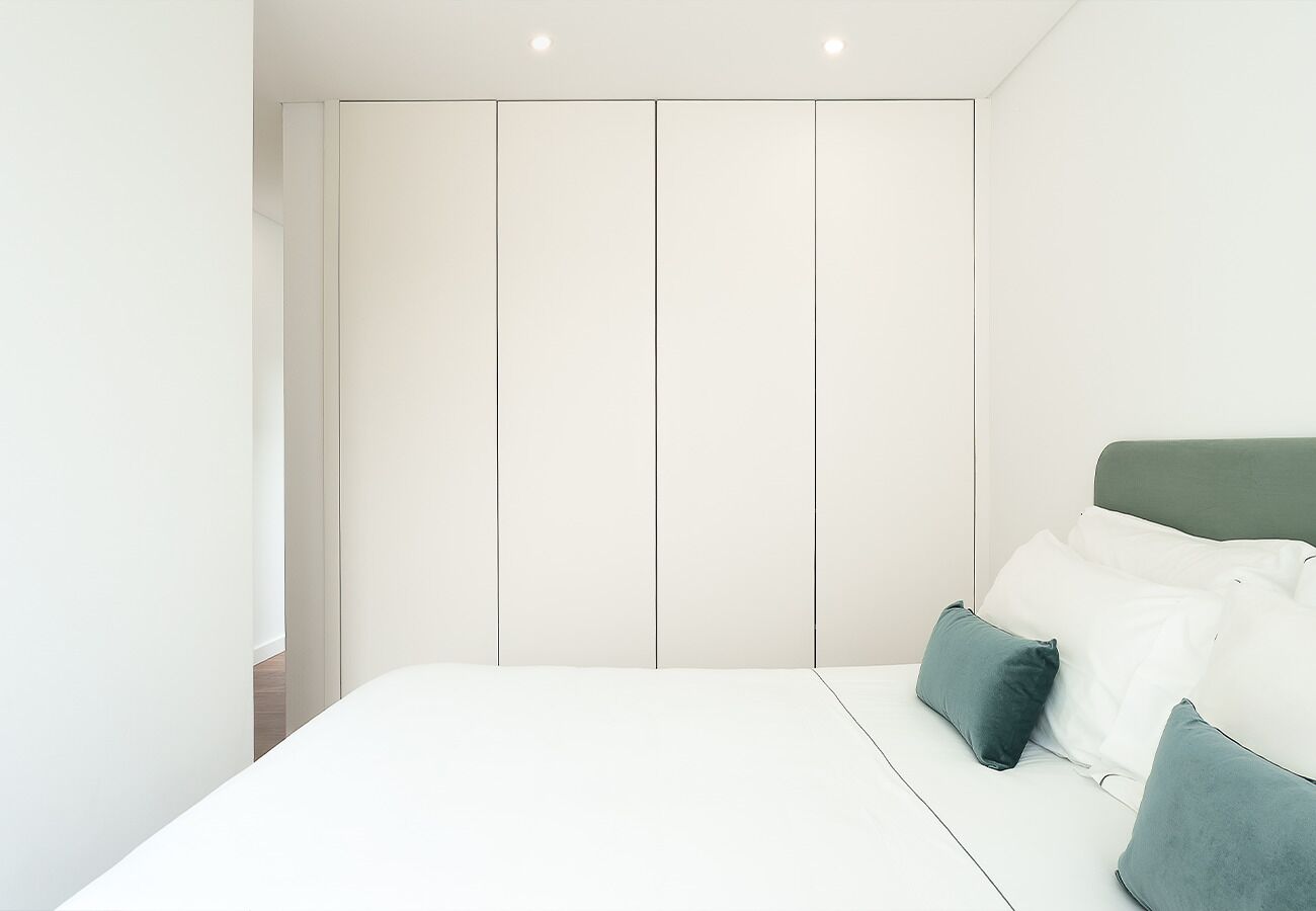 A bedroom with a bed, a green headboard, and white bedding.