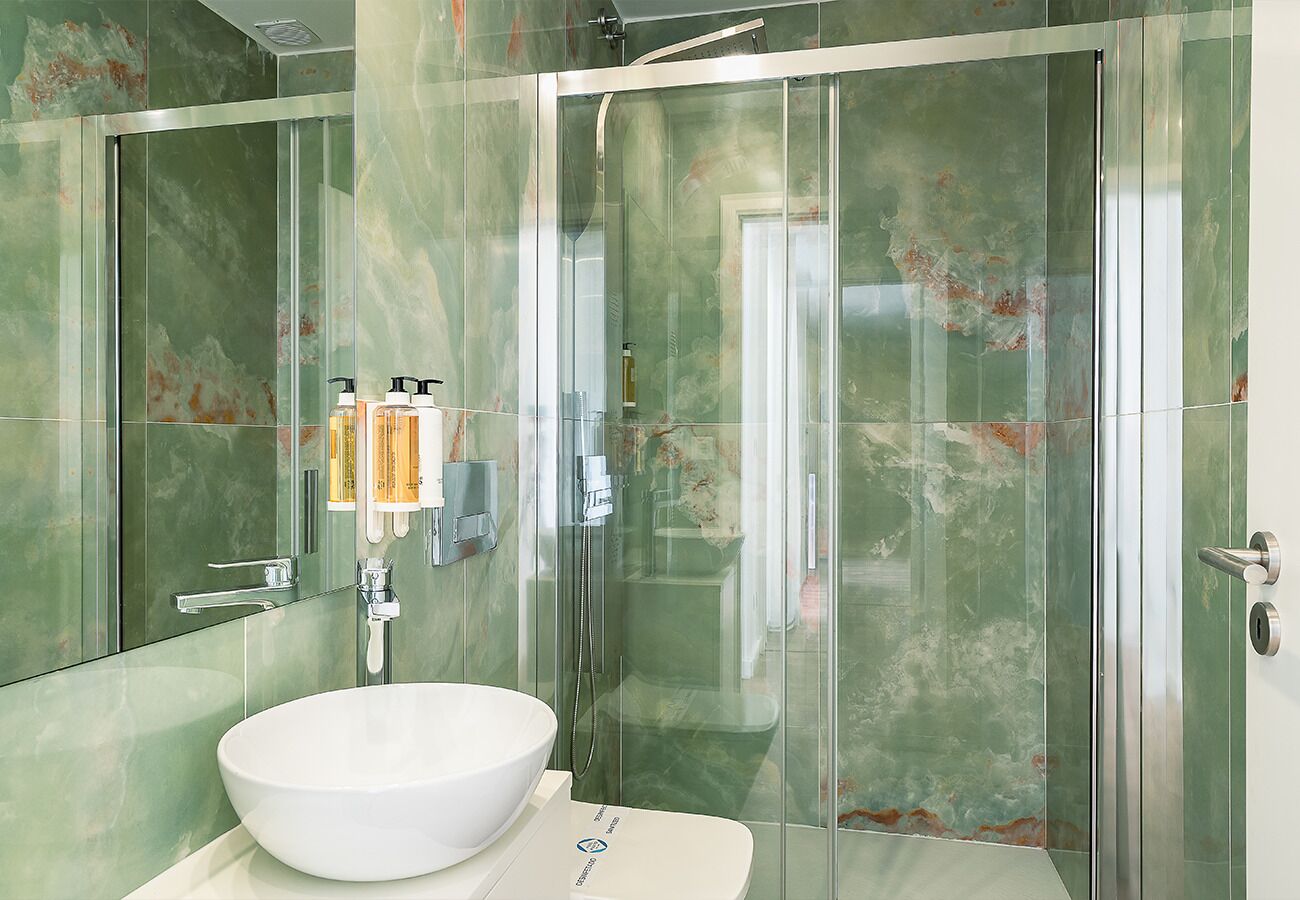 Une salle de bain moderne avec une douche à parois de verre, un lavabo blanc et un pare-feu en marbre.