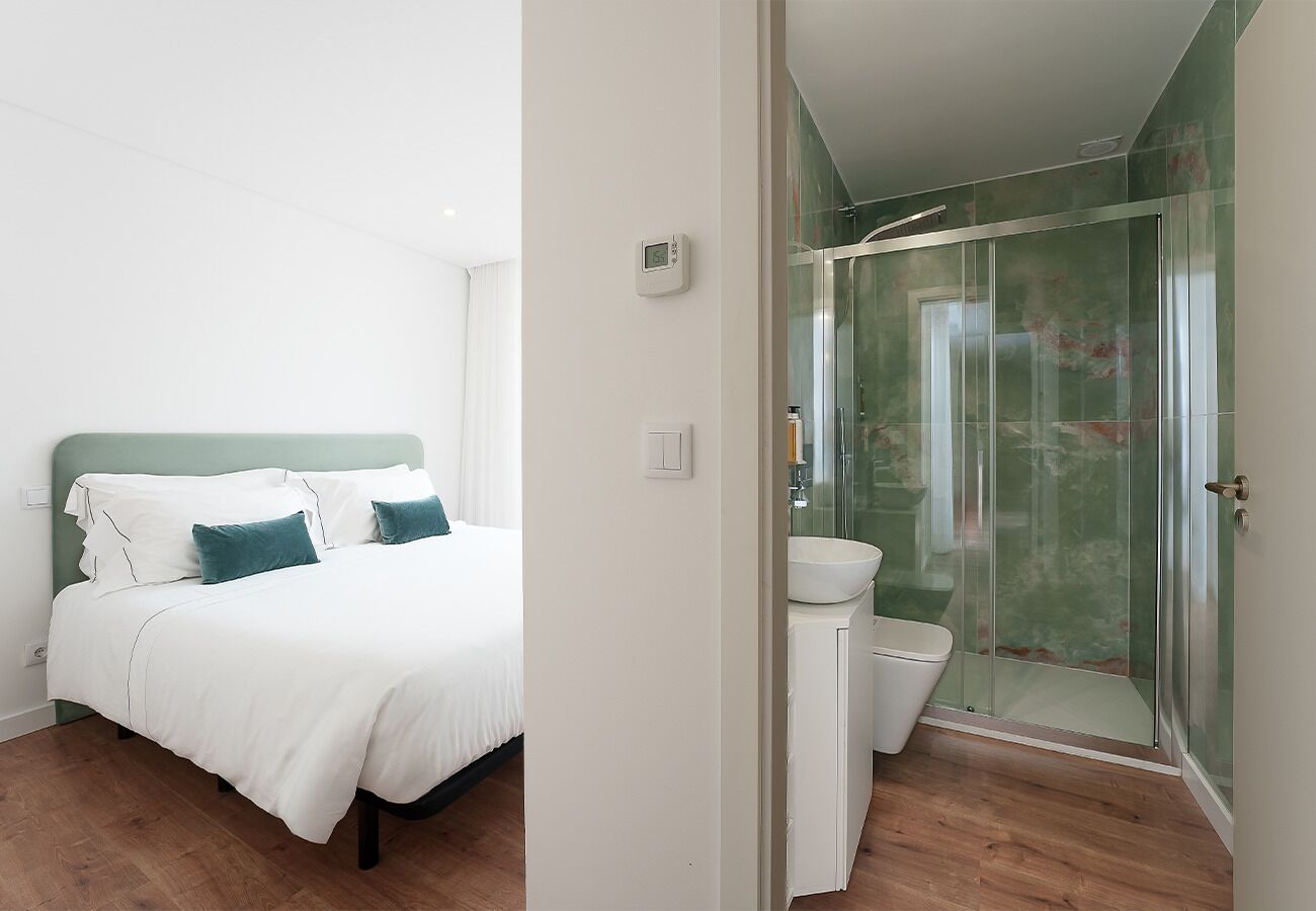A bedroom with a bed, a bedside table, and a glass-enclosed shower area.