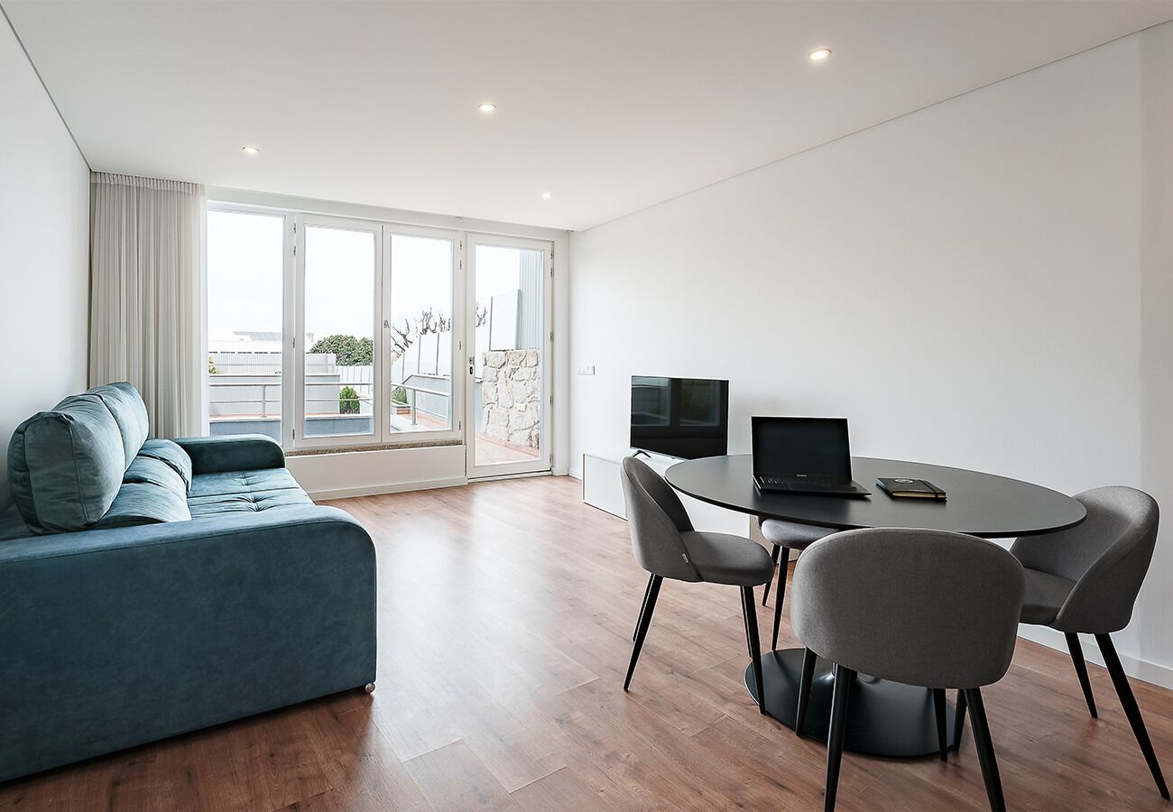 A modern living room with a sofa, a dining table with chairs, a laptop, and a television.