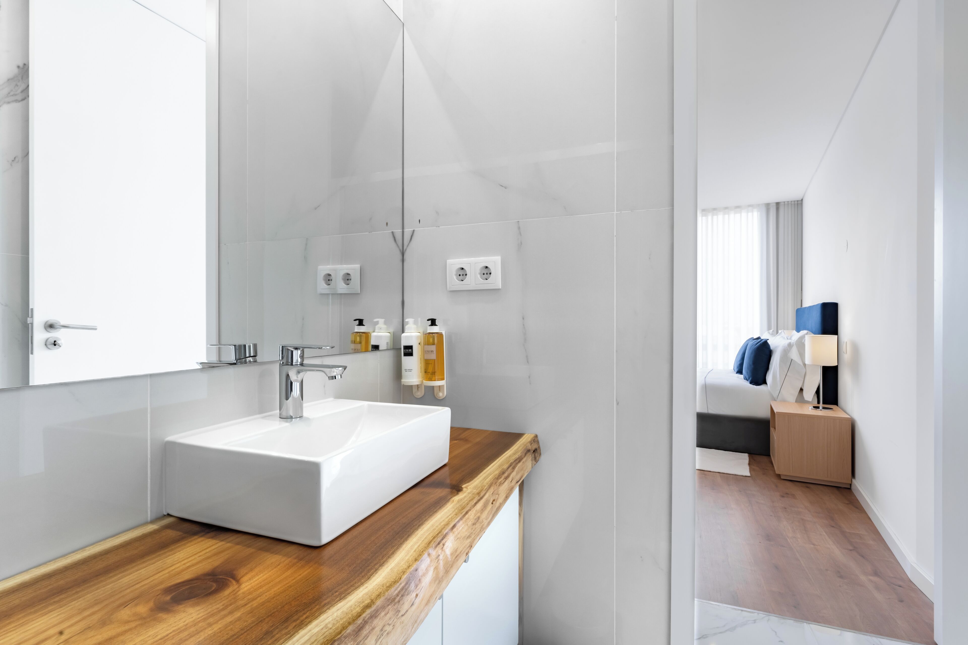 A modern bathroom with a white sink, wooden countertop, and a large mirror.