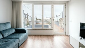 Ein modernes Wohnzimmer mit grauem Sofa, einem Flachbildfernseher und einer großen Glastür, die auf einen Balkon im Freien führt.