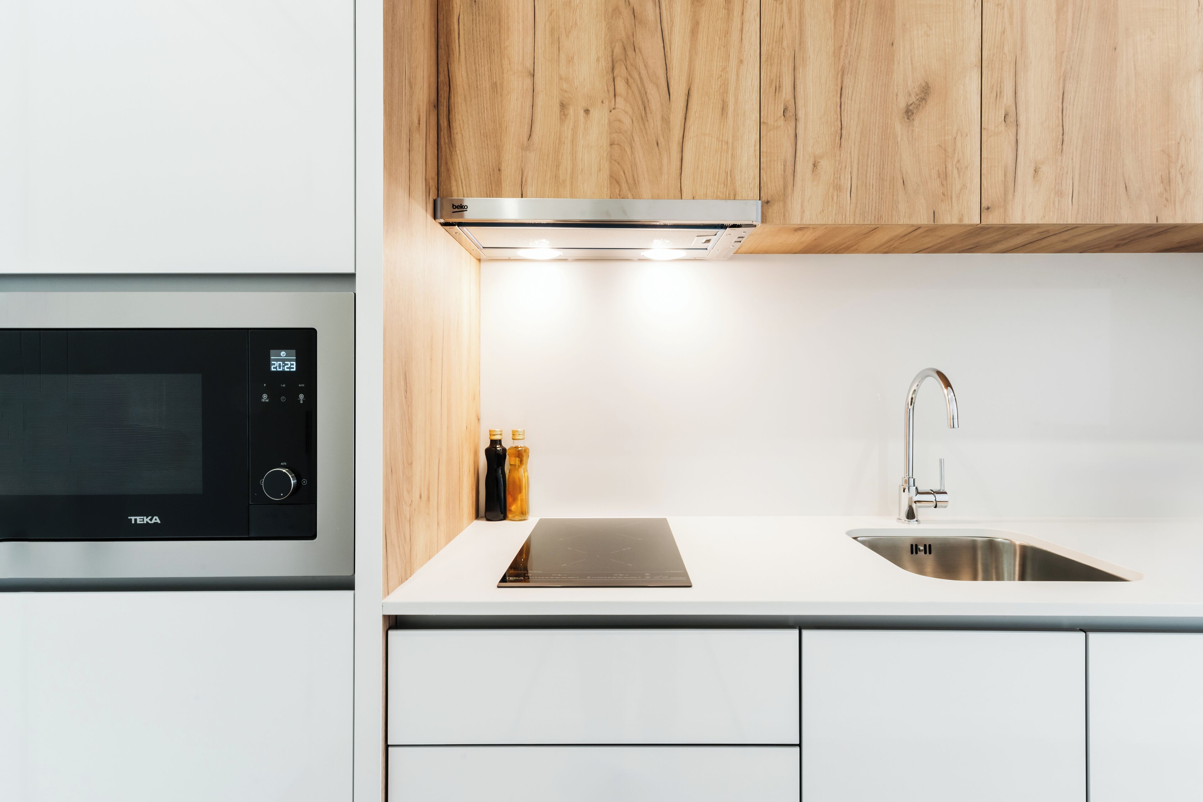 Una cocina moderna con microondas integrado, pileta de acero inoxidable y muebles de madera.