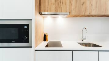 Una cocina moderna con microondas integrado, pileta de acero inoxidable y muebles de madera.