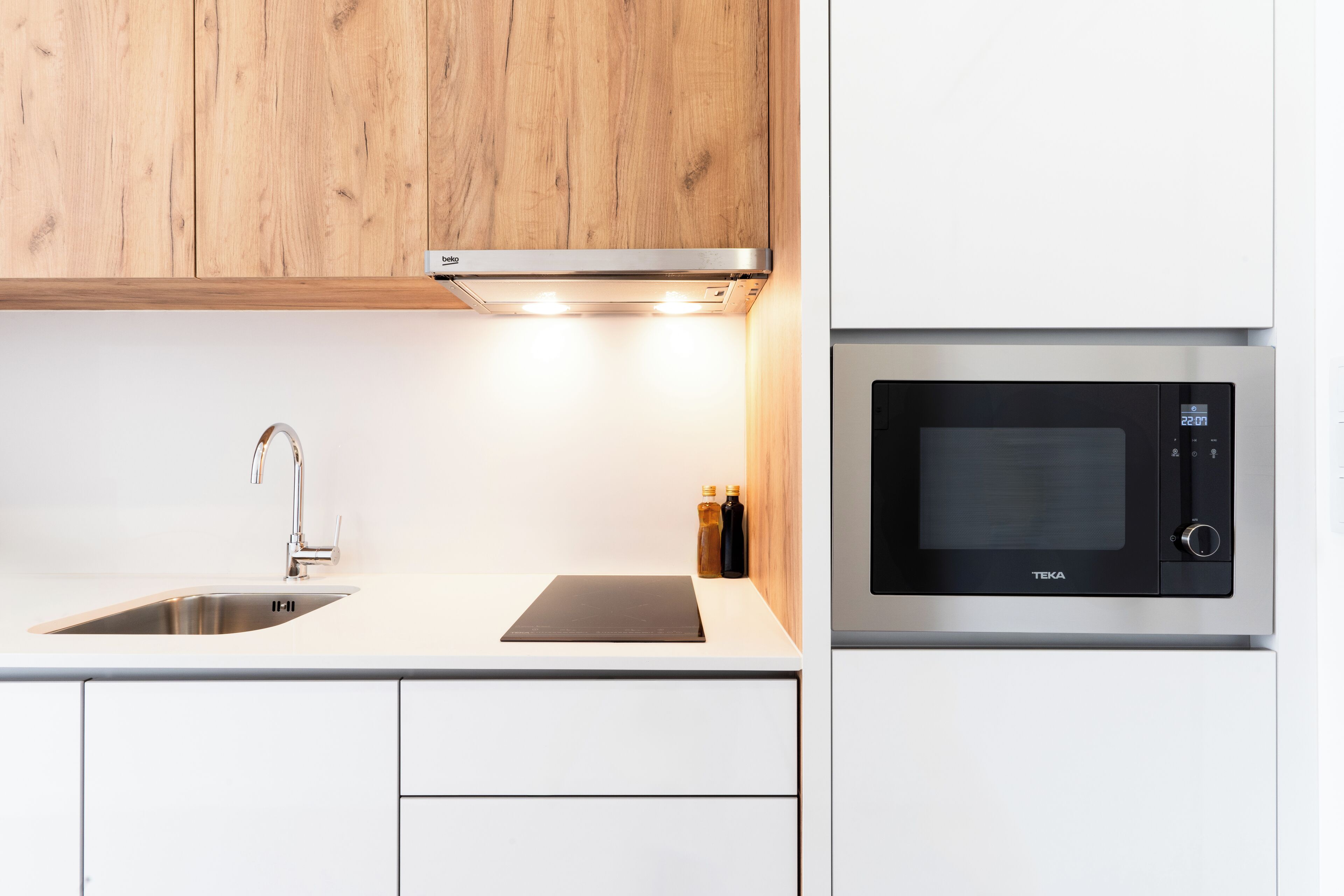 Una cocina moderna con un lavamanos de acero inoxidable, una placa de inducción negra y un horno microondas integrado.