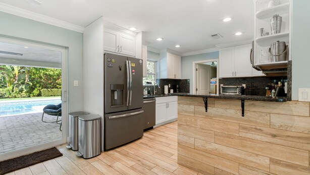 A modern kitchen with a built-in oven, stainless steel appliances, and a view of a swimming pool. - Charming 4-Bedroom Beach Bungalow with Idyllic Pool & Backyard (Tequesta)