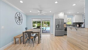 A spacious kitchen with wooden flooring, a dining area with a bench, and a view of a pool through glass doors. - Charming 4-Bedroom Beach Bungalow with Idyllic Pool & Backyard (Tequesta)