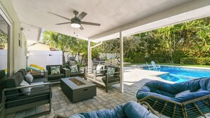 An outdoor patio with a pool, seating areas, and a ceiling fan. - Charming 4-Bedroom Beach Bungalow with Idyllic Pool & Backyard (Tequesta)