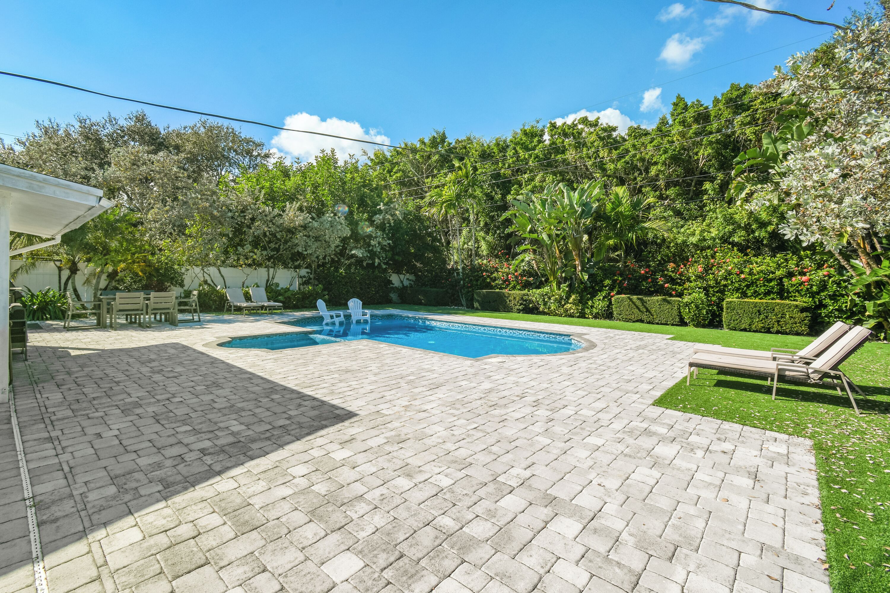 A backyard with a swimming pool, patio furniture, and lush greenery.