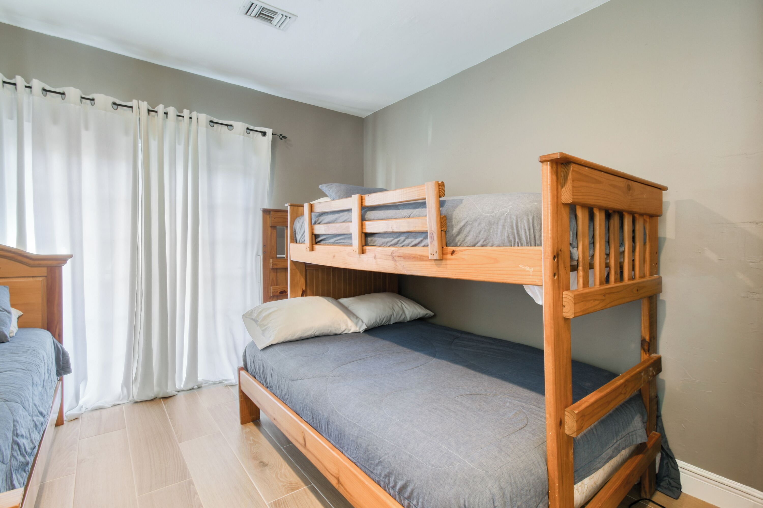 Habitación con literas, cabecera de madera, una cama individual con colchón gris y una cortina que cubre una ventana.