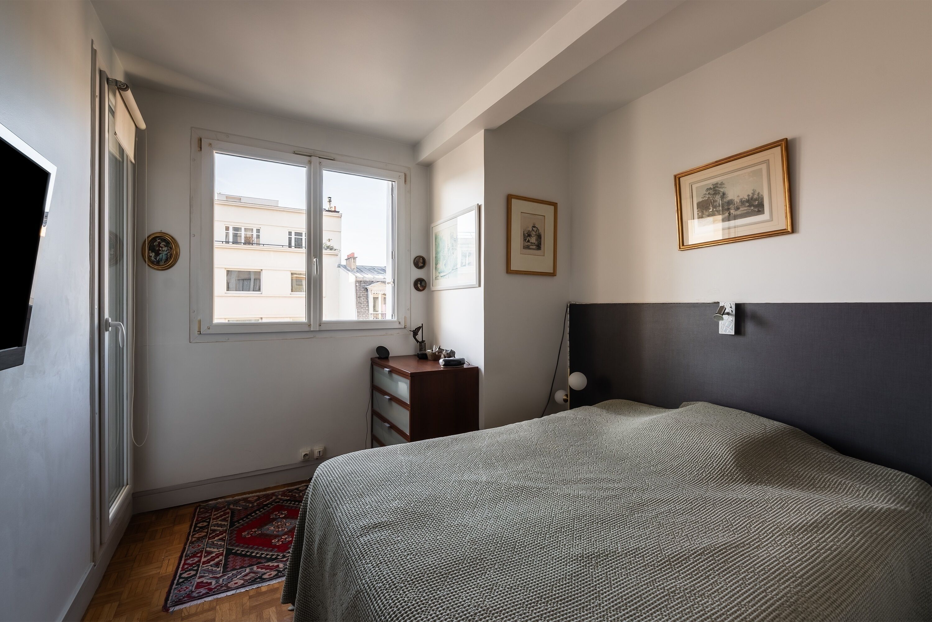 Een slaapkamer met een bed, een dressoir, een raam en een deur.