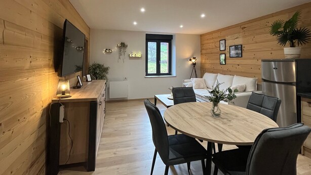 A modern kitchen with wooden walls, a dining area with a round table and chairs, and a built-in TV.