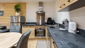 A modern kitchen with wooden cabinetry, a stainless steel range hood, a built-in oven, and a coffee machine.