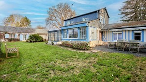 A two-story house with a blue exterior, a front yard with a bench, and a small garden area.