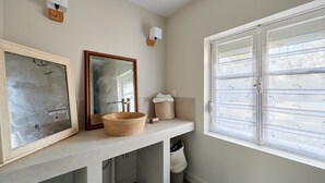 A bathroom with a large mirror, a wooden bowl sink, a towel holder, and a window with blinds.