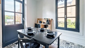 Un comedor con una mesa preparada para cuatro, una cocina al fondo y ventanas amplias con vistas al exterior.