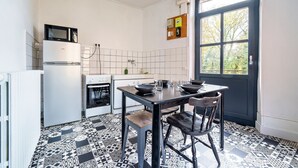 Una cocina con una mesa de comedor, sillas, un refrigerador, un horno y un ventanal con vistas a árboles.