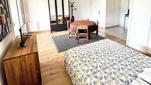 Een slaapkamer met een bed, bureau, stoel, tafel met stoelen, kapstok en een deur.