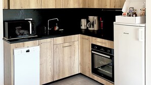Een compacte keuken met houten kastjes, een zwart aanrecht, een witte vaatwasser, een inbouwoven en een witte koelkast.