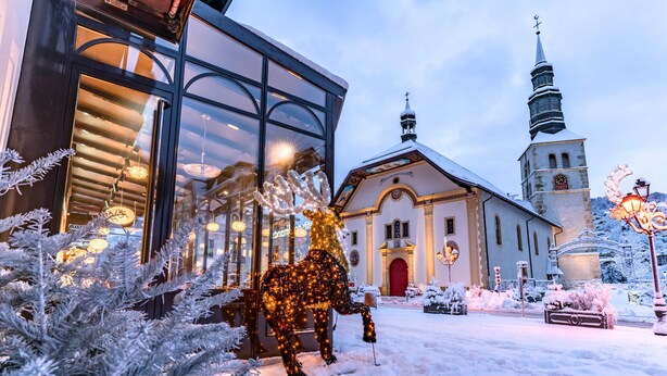 Een met sneeuw bedekte kerk met een kerktoren, een modern gebouw met grote ramen, en een kerstboom sculptuur.