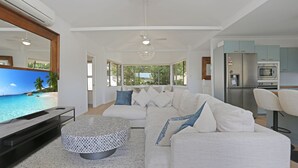 A modern living room with a large TV, a white sofa, and a dining area.
