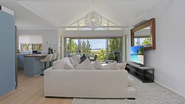 A modern living room with a sofa, TV, and a balcony with a view.