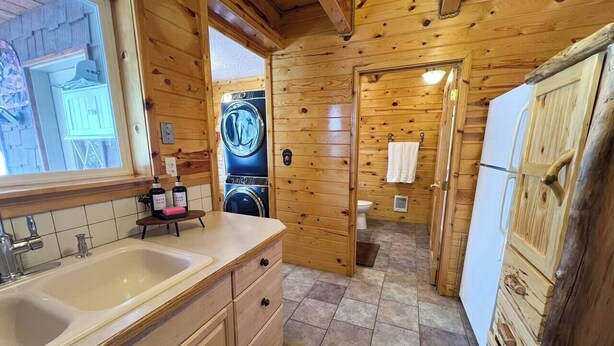 A wooden cabin interior with a kitchen area featuring a sink, a washing machine, and a refrigerator.