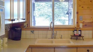 A wooden cabin-style kitchen with a window, sink, cabinets, and a stove.