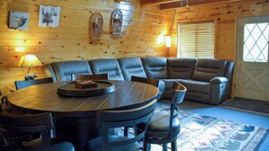 A cozy cabin interior with a round dining table, leather sofa, and a ceiling fan.