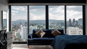 A modern bedroom with a large window, a dark blue sofa, and a bed.