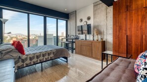 Ein modernes Schlafzimmer mit Bett, Fernseher, Holzschrank und großem Fenster mit Blick auf die Stadt.