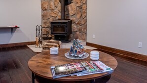 A cozy room with a stone wall, a fireplace, a small Christmas tree, and a round wooden table with magazines.