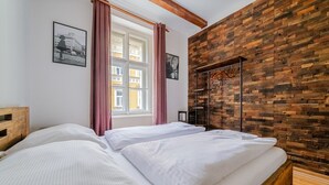 A bedroom with two beds, a window with curtains, and a wooden wall with a coat rack.