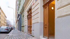 A cobblestone street with buildings on either side, a parked car, and a visible entrance to a building with a wooden door.