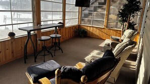 A cozy room with a wooden interior, a ceiling fan, a TV mounted on the wall, and a large window offering a view of the outdoors. - Charming 2-bedroom house with WiFi, AC on Knife Lake in Mora Minnesota.  (Mora)
