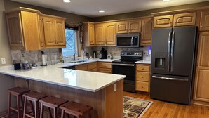 A modern kitchen with wooden cabinets, stainless steel appliances, and a large island with bar stools. - Charming 2-bedroom house with WiFi, AC on Knife Lake in Mora Minnesota.  (Mora)