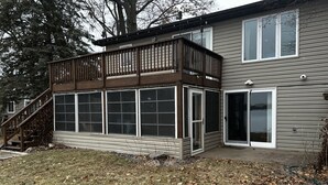 A two-story house with a wooden deck and a large sliding glass door. - Charming 2-bedroom house with WiFi, AC on Knife Lake in Mora Minnesota.  (Mora)