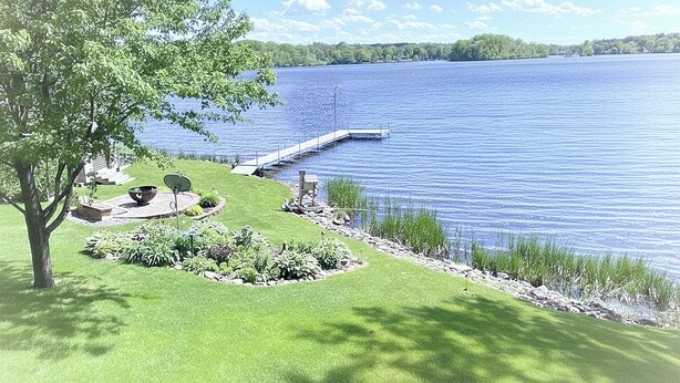 A lakeside property with a dock extending into the water, surrounded by well-maintained grass and a variety of plants. - Charming 2-bedroom house with WiFi, AC on Knife Lake in Mora Minnesota.  (Mora)